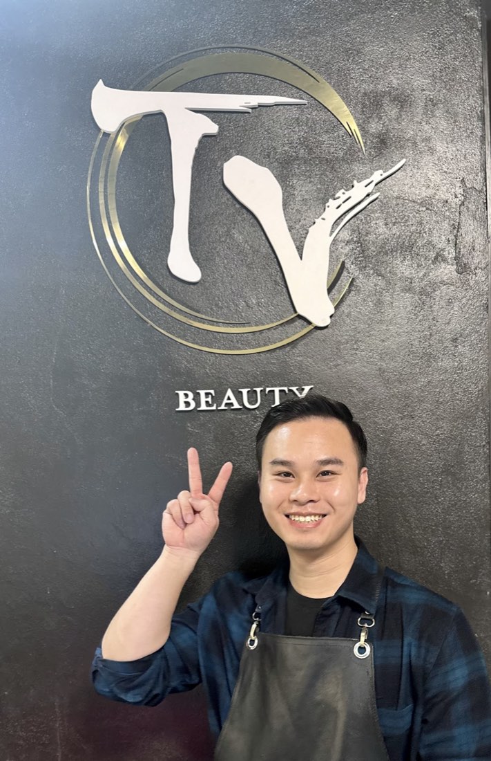 The barber at TV Beauty in front of the salon's gold logo